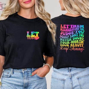 May include: Two black t-shirts with rainbow text. The first shirt says "Let them" with a heart. The second shirt says "Let them misunderstand you, judge you, gossip about you, never doubt your worth, your beauty. *Keep Shining*"