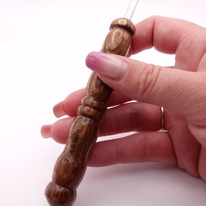 May include: A wooden crochet hook with a dark brown finish. The hook has a rounded handle with a textured design and a silver metal hook. The size is marked as 7 / 4.5 mm.