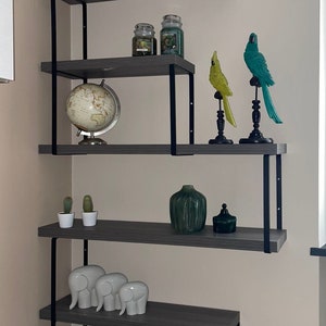 May include: A gray and black corner shelf unit with various decorative items. The shelves display a white skull, candles, bird figurines, a globe, cacti, vases, elephant figurines, books, and a rose arrangement.