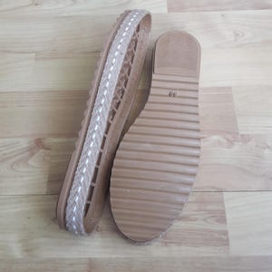May include: Two tan shoe soles. One sole is a strip with a white lace design. The other sole is a solid piece with a ridged bottom. The number 38 is visible on the solid sole.