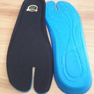 May include: Two insoles, one black and one blue, are displayed. The black insole has a split toe design and a gold emblem. The blue insole has a contoured design with the size 42-43 printed on it. The insoles are designed for comfort.