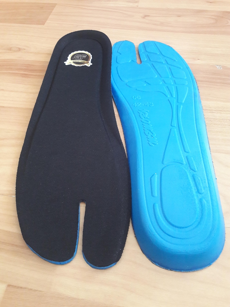 May include: Two insoles, one black and one blue, are displayed. The black insole has a split toe design and a gold emblem. The blue insole has a contoured design with the size 42-43 printed on it. The insoles are designed for comfort.