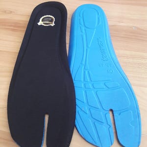 May include: Two tabi-style insoles, one black and one blue, are displayed on a wooden surface. The black insole has a logo and a blue trim. The blue insole has a textured design and text that reads "12-13".