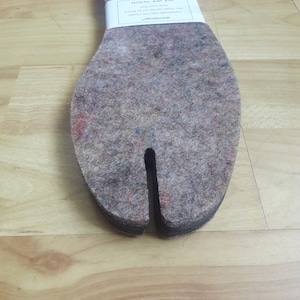 May include: A pair of gray felt shoe insoles with a split toe design. The insoles are designed to help keep your feet warm and dry. The text on the label reads "Handmade felt insoles. This insole can be cut to fit your size. Use over your regular insoles."