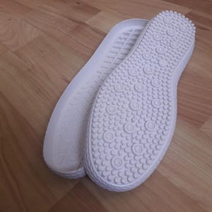 Op de afbeelding: Twee witte rubberen zool met een textuurpatroon. E&eacute;n zool heeft een golvend patroon en de andere heeft een patroon van kleine cirkels.