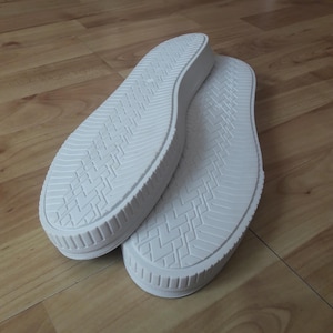 Puede incluir: Dos suelas de zapatos blancas con patrones texturizados y un borde elevado. Las suelas están hechas de un material gomoso y están diseñadas para zapatillas deportivas o zapatos casuales. Las suelas están limpias y parecen nuevas.