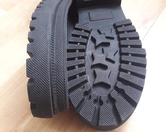 Könnte beinhalten: Nahaufnahme der schwarzen Gummisohlen eines Schuhpaares. Die Sohlen haben ein strukturiertes Muster mit erhabenen Rippen und Sternen.