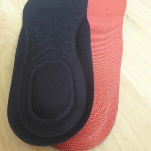 May include: Two pairs of black and red fabric insoles with a split toe design. The insoles are made of a soft, textured material.