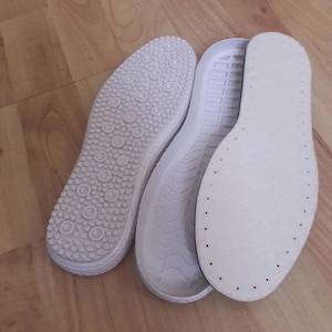 Op de afbeelding: Drie witte schoen inlegzolen, een met een textuur, een met een golvend patroon en een met een glad oppervlak met kleine gaatjes.