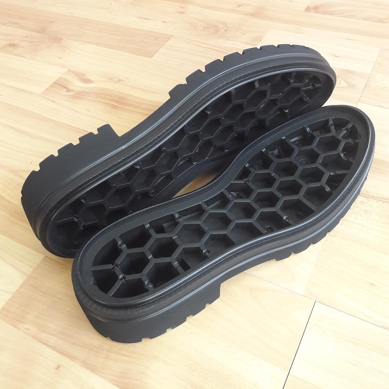 K&ouml;nnte beinhalten: Zwei schwarze Schuhsohlen mit einem robusten Profilmuster und einem Wabenmuster im Inneren. Die Sohlen bestehen aus einem strapazierf&auml;higen Material und sind f&uuml;r Stiefel oder strapazierf&auml;higes Schuhwerk konzipiert.
