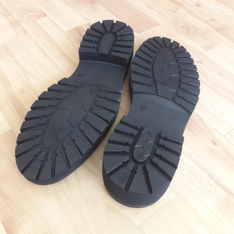 K&ouml;nnte beinhalten: Ein Paar schwarze, klobige Schuhsohlen mit tiefen Profilmustern. Die Sohlen bestehen aus einem strapazierf&auml;higen Material und sind f&uuml;r Traktion ausgelegt. Die Stiefel sind wahrscheinlich f&uuml;r den Au&szlig;enbereich gedacht.