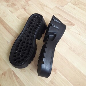 May include: Two black platform shoe soles. One sole features small holes, the other has a ridged, textured design. The soles are made of a durable material and are designed for footwear.