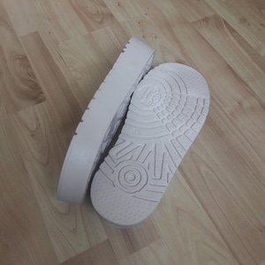 May include: Two light pink platform soles. One sole is lying flat, showing the textured bottom with a circular design. The other sole is on its side, revealing the platform's height and a ridged edge.