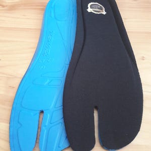 May include: Two split-toe insoles. One is bright blue with text and size markings, the other is black with a gold emblem. The insoles are designed to fit shoes with a split toe design.