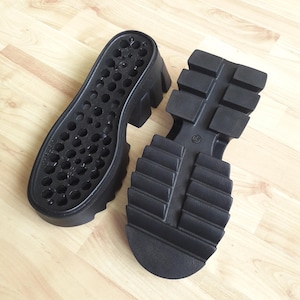 May include: Two black platform shoe soles. One sole features small holes, the other a treaded design with the number 38 embossed. These durable soles are designed for footwear and are made of a robust material.