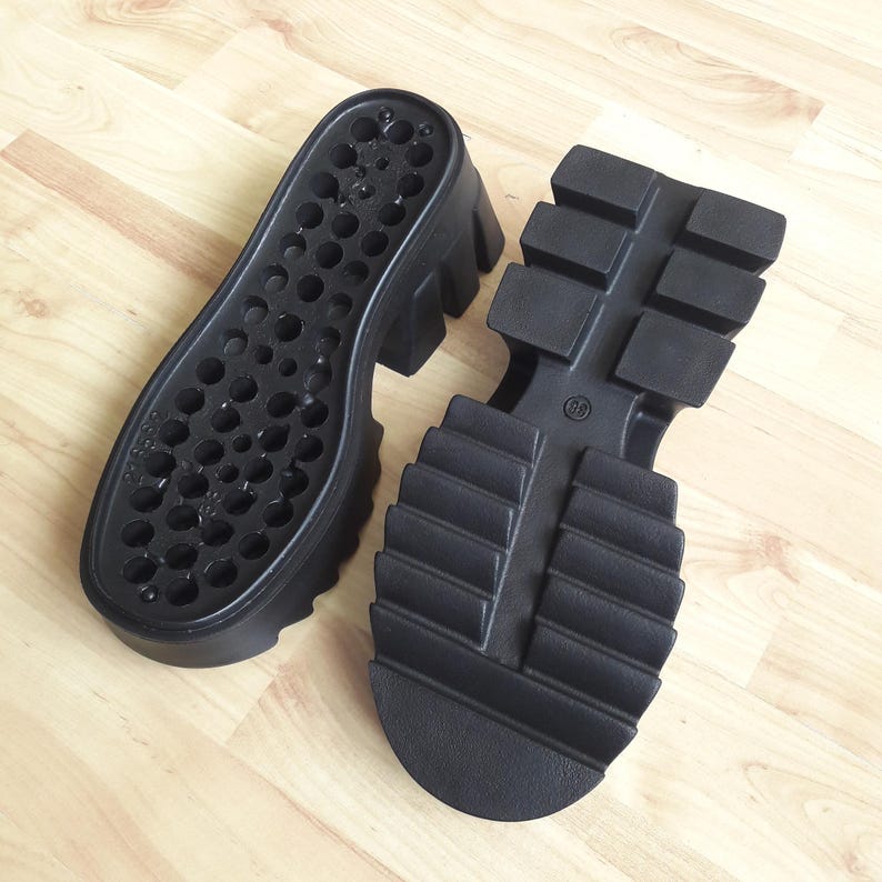 May include: Two black platform shoe soles. One sole features small holes, the other a treaded design with the number 38 embossed. These durable soles are designed for footwear and are made of a robust material.