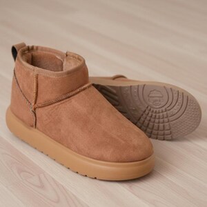 May include: A pair of brown ankle boots with a rounded toe and a thick sole. The boots have a soft, suede-like texture and a light brown sole. One boot is upright, and the other is lying on its side, showing the tread.