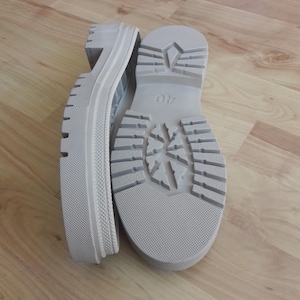 Puede incluir: Par de suelas de bota de plataforma gris claro con un diseño de banda de rodadura grueso. Las suelas son nuevas y sin usar, con una marca de talla 40. Las botas están hechas de un material duradero.