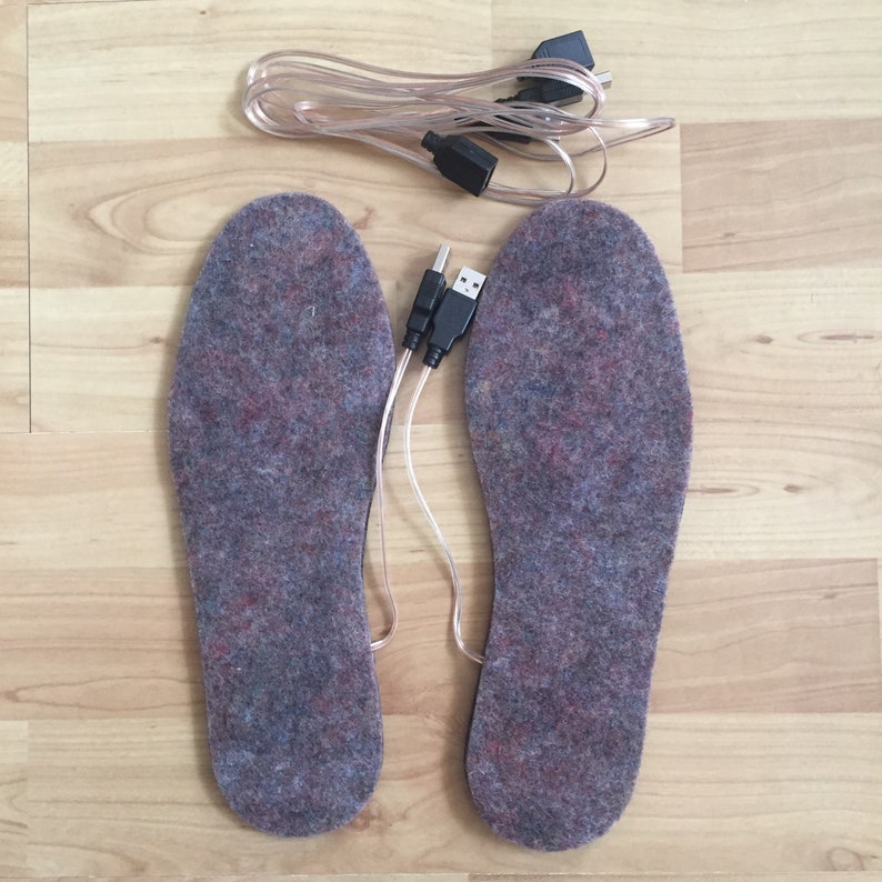 K&ouml;nnte beinhalten: Ein Paar graue Heizsohlen mit USB-Kabeln. Die Sohlen bestehen aus einem weichen, flauschigen Material.