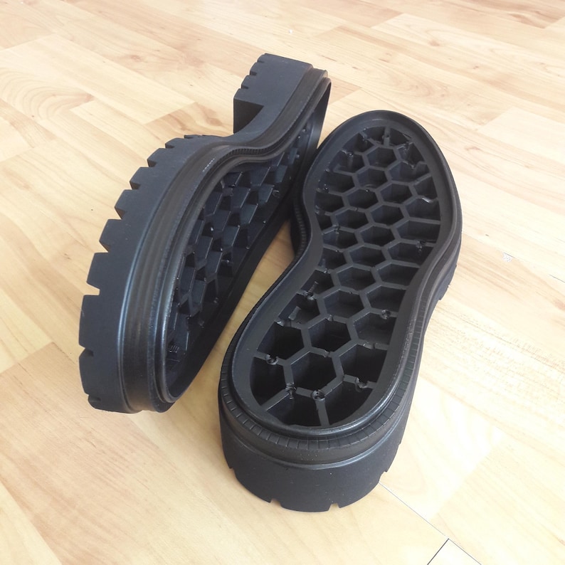 K&ouml;nnte beinhalten: Zwei schwarze Schuhsohlen mit einer dicken, geriffelten Plattform und einem Wabenmuster auf der Innensohle. Die Sohlen bestehen aus einem strapazierf&auml;higen Material und sind f&uuml;r Stiefel oder &auml;hnliches Schuhwerk konzipiert.