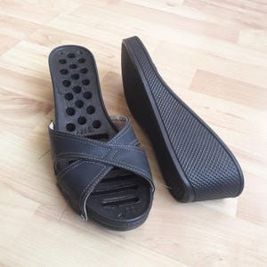 Puede incluir: Sandalias de cuña negras con un diseño de correas entrecruzadas. Las sandalias tienen una suela texturizada y una serie de agujeros en la plantilla. Talla 38.