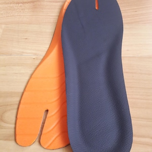 May include: Two tabi-style insoles. One is orange, the other is dark blue. The insoles have a split-toe design, and are made of a textured material. The insoles are designed to fit the traditional Japanese split-toe footwear.