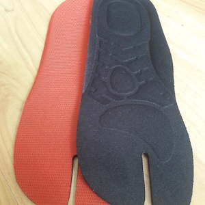 May include: Two pairs of black and orange fabric insoles with a split toe design. The insoles are made of a soft, flexible material and have a textured surface.
