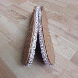 Puede incluir: Un par de sandalias estilo alpargata de color beige, con un ribete de yute tejido y suelas texturizadas. Las sandalias se muestran dobladas, revelando las costuras blancas a lo largo de los bordes. Las suelas tienen un patrón geométrico.