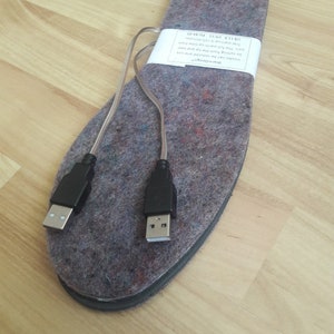 K&ouml;nnte beinhalten: Ein Paar USB-betriebene Heizsohlen mit grauem Stoff und schwarzen Kabeln. Das Etikett lautet "WarmDesign Insol des can be reduced one size by cutting from the tip and het part. The full warm-up time from first start-up is 15 minutes. USIIS KEZEU 44-45"
