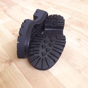 May include: Black platform boots with a chunky sole. The boots have a treaded outsole for grip and a thick platform. The boots are made of a durable material and are designed for comfort and style.