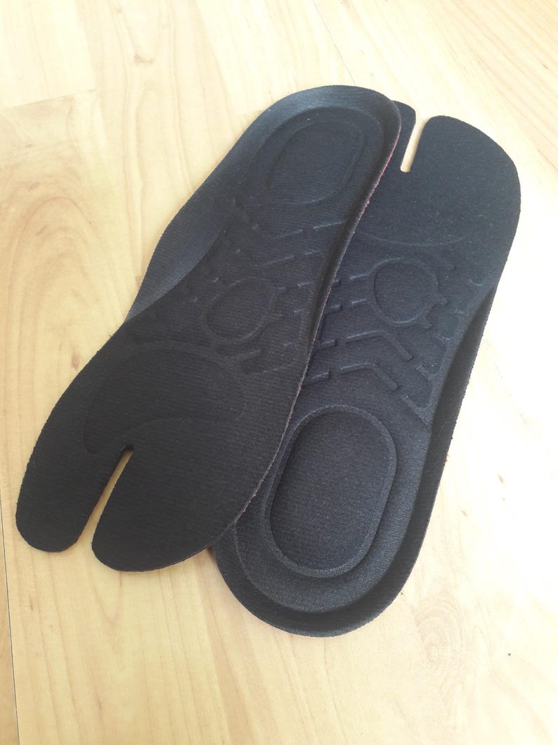 May include: A pair of black fabric insoles with a textured surface. The insoles are designed to fit into shoes and provide support and comfort.