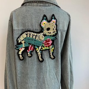 May include: A black and white embroidered patch of a French Bulldog skeleton with colorful flowers and the text "French Bulldog" on a denim jacket.