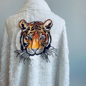 Puede incluir: Chaqueta blanca de lentejuelas con un diseño de tigre bordado en la espalda.