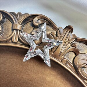 Peut inclure: Une &eacute;toile argent&eacute;e en forme d'&eacute;toile avec des strass transparents. L'&eacute;toile est sur une surface dor&eacute;e.