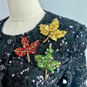 May include: Black sequined jacket with three embroidered leaf appliques. The leaves are red, green, and gold.