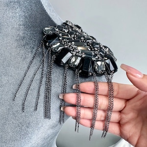 May include: A black and silver embellished shoulder patch with a fringe of black chains.