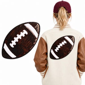 Puede incluir: Una chaqueta universitaria con cuerpo de lana color crema y mangas de cuero marrón, que presenta un gran parche de fútbol americano con lentejuelas en la espalda. Un parche de lentejuelas a juego se muestra por separado a la izquierda.