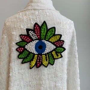 May include: White sequined jacket with a colorful embroidered eye design on the back.