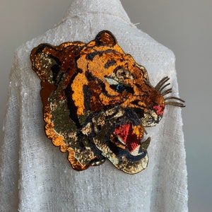 May include: A white sequined jacket with a large, gold, orange, and black tiger applique on the back.