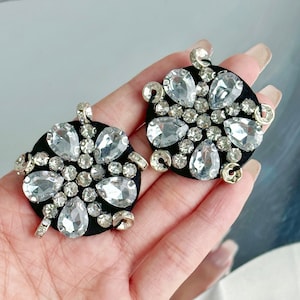 Pode incluir: Dois círculos de tecido preto com strass prateados e transparentes dispostos em forma de flor.