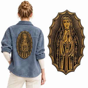 May include: A blue denim button-down shirt featuring a large, embroidered patch on the back. The patch depicts a figure in a hooded robe with hands clasped in prayer, rendered in gold thread against a black background with a sunburst border.