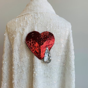 May include: A white sequined jacket with a red and silver sequined heart appliqué on the back.