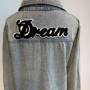 May include: A light blue denim jacket with a black and white embroidered patch that says "Dream" on the back.