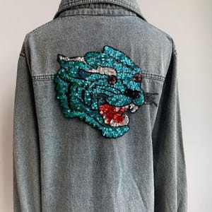 Op de afbeelding: Een blauwe denimjas met een groot gestikt panterontwerp op de rug.