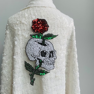 May include: White jacket with a sequined skull and rose embroidered on the back. The skull is gray and the rose is red with green leaves.