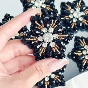 Peut inclure: Des embellissements en forme d'étoile noire avec des accents de perles dorées et un grand strass transparent au centre.