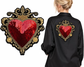 Puede incluir: Un parche grande en forma de corazón con lentejuelas rojas y bordados dorados sobre fondo negro, mostrado como artículo independiente y aplicado en la espalda de una camisa negra de manga larga con cuello y corte holgado.