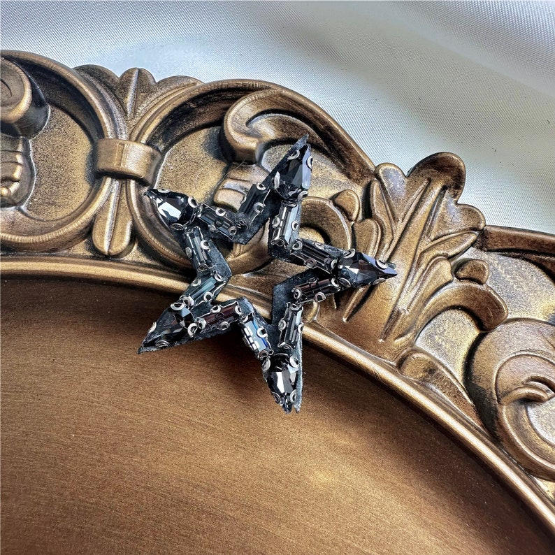 Peut inclure: Une &eacute;toile noire en forme d'&eacute;toile avec des strass. L'&eacute;toile est sur un fond dor&eacute;.