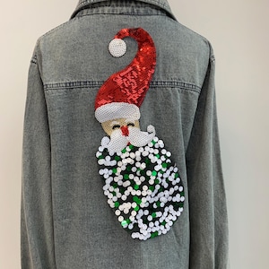 May include: A denim jacket with a sequined Santa Claus design on the back. The Santa is wearing a red hat and has a white beard and green and white sequins for his body.