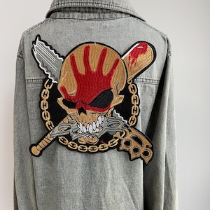 May include: A gray denim jacket featuring a large embroidered patch on the back. The patch depicts a skull with a red handprint, a baseball bat, a knife, brass knuckles, and a chain.